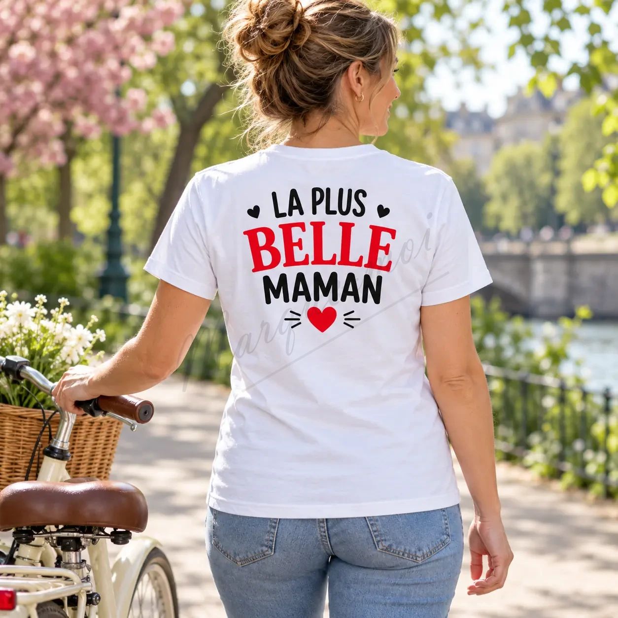 Femme vue de dos dans un jardin fleuri, portant un t-shirt blanc avec l’inscription « La plus belle maman » en noir et rouge.