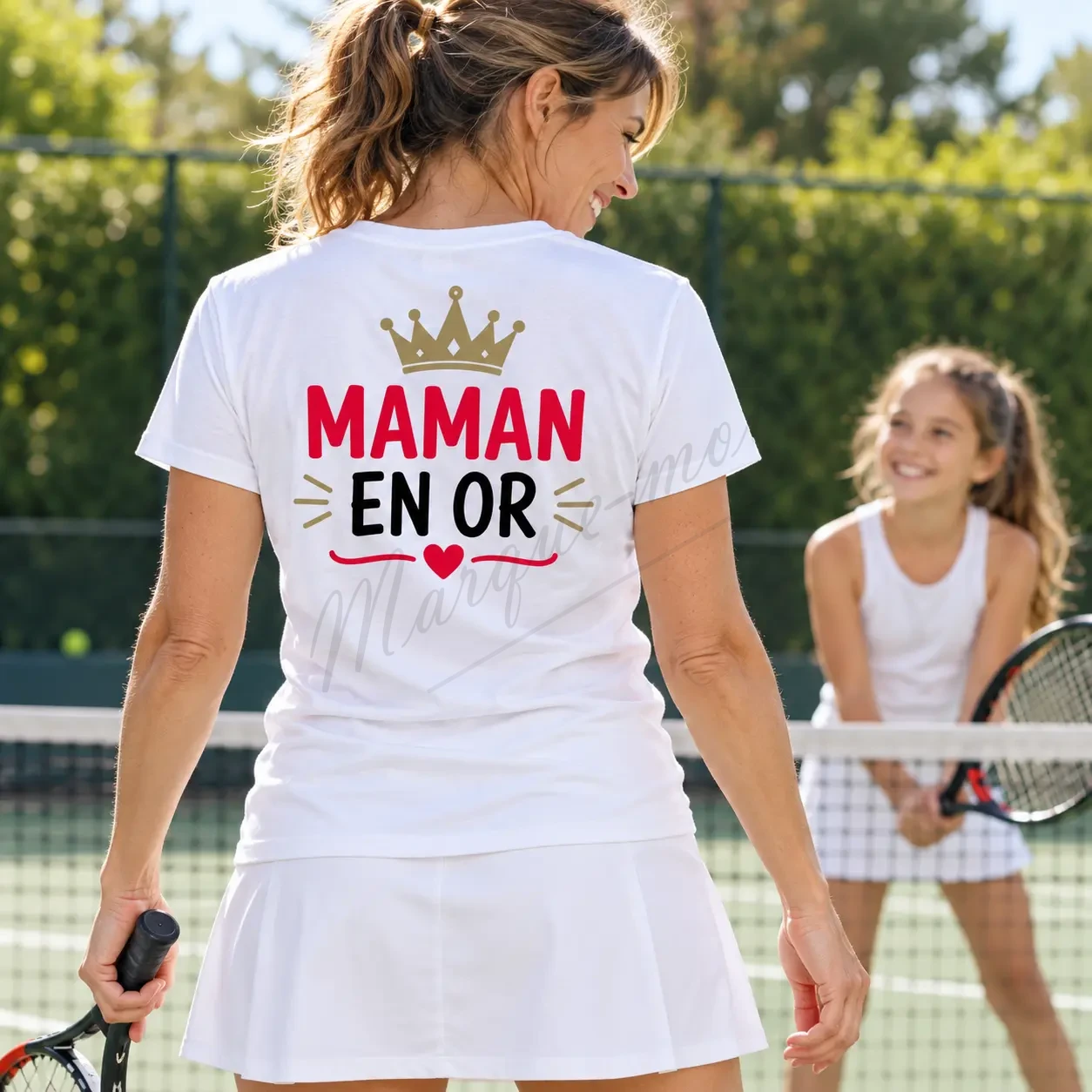 Femme vue de dos dans un jardin, portant un t-shirt blanc « Maman en or » avec une couronne dorée et un cœur rouge.