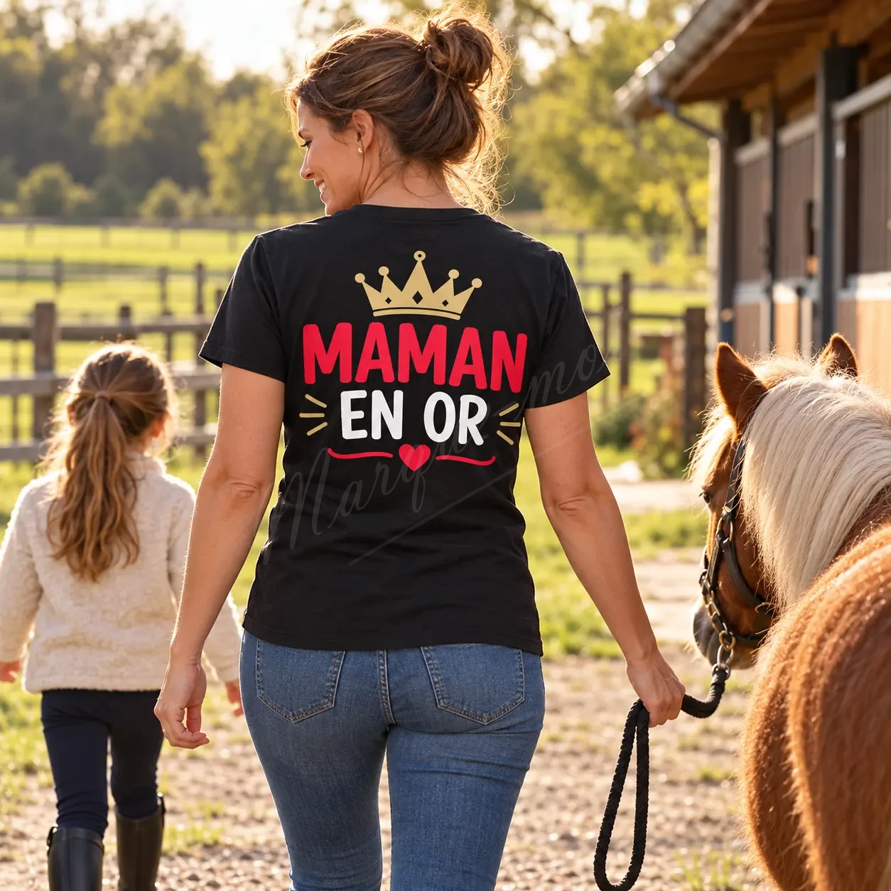 Femme vue de dos dans un jardin, portant un t-shirt noir « Maman en or » avec une couronne dorée et un cœur rouge.