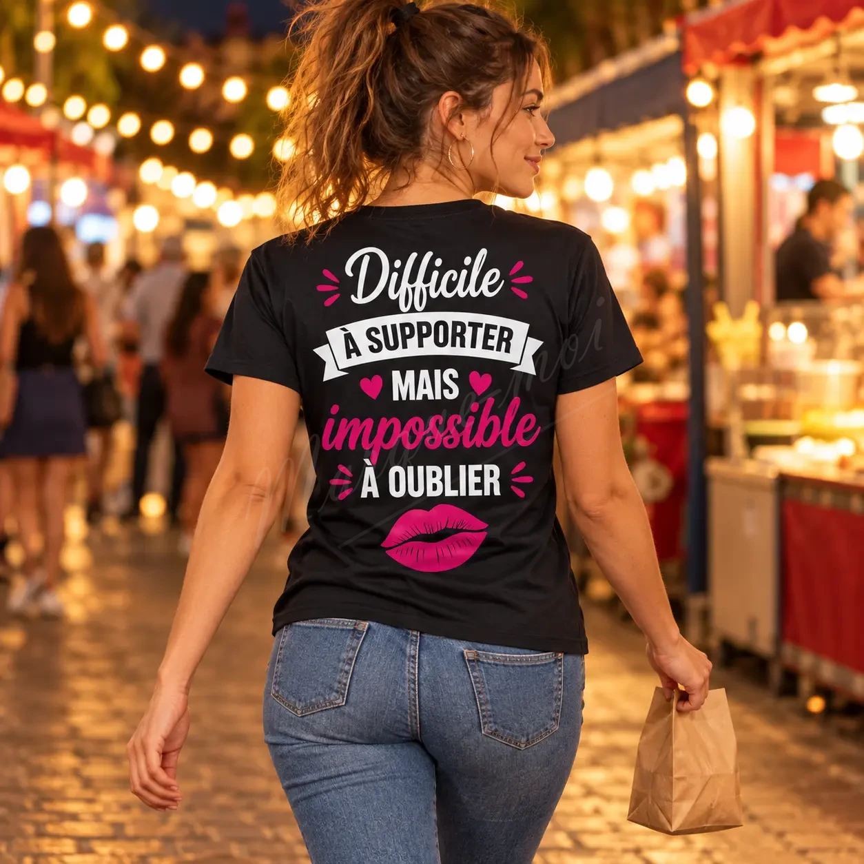 Femme vue de dos sous des guirlandes lumineuses, portant un t-shirt noir « Difficile à supporter mais impossible à oublier ».