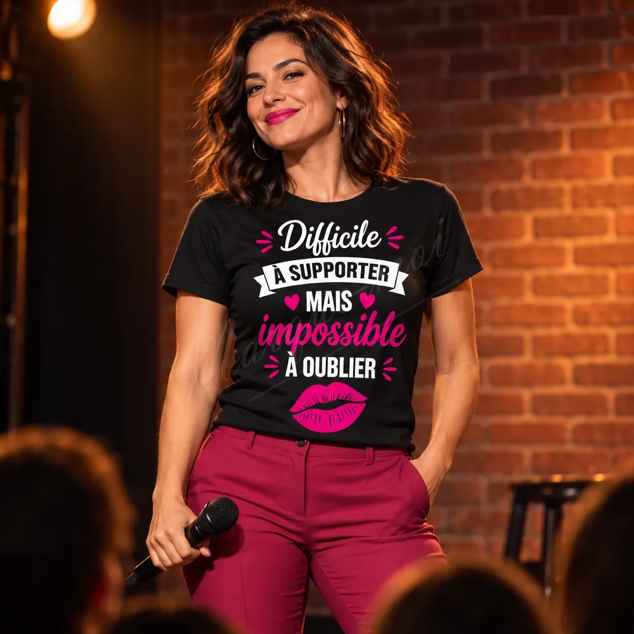 Femme devant un mur de briques, portant un t-shirt noir « Difficile à supporter mais impossible à oublier » avec un motif blanc et rose.