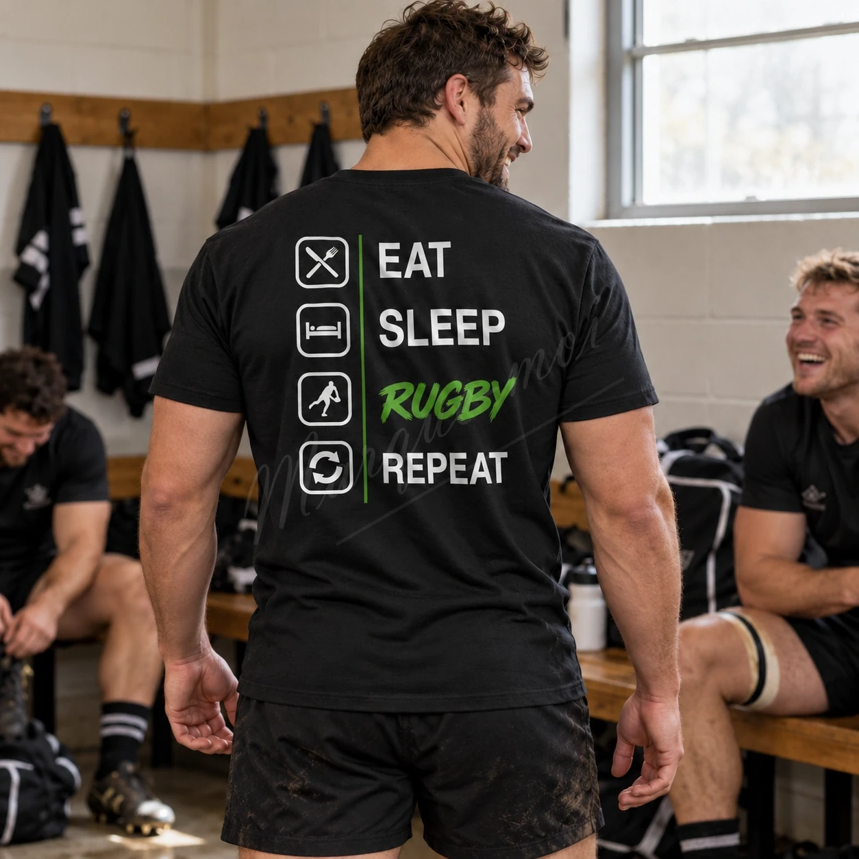 Homme vu de dos dans un vestiaire portant un t-shirt noir « Eat Sleep Rugby Repeat », au motif blanc et vert clair.