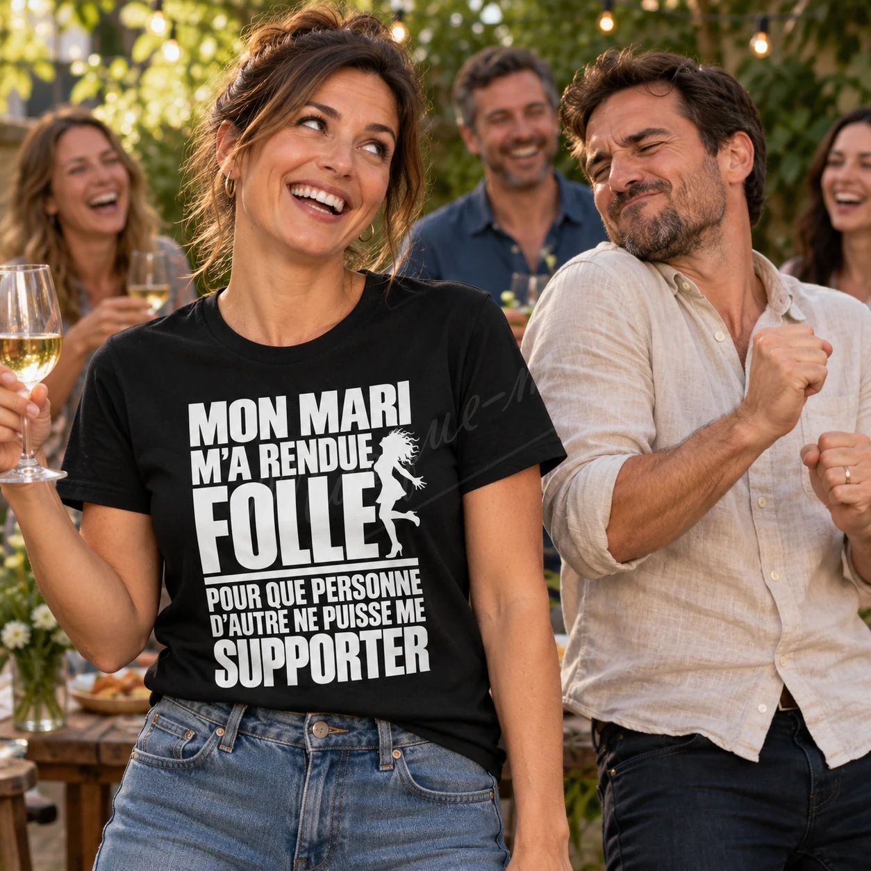 Femme dans un jardin portant un t-shirt noir « Mon mari m’a rendue folle pour que personne d’autre ne puisse me supporter », entourée de personnes.