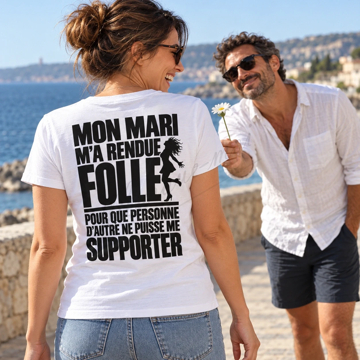 Femme vue de dos en bord de mer, portant un t-shirt blanc « Mon mari m’a rendue folle pour que personne d’autre ne puisse me supporter ».