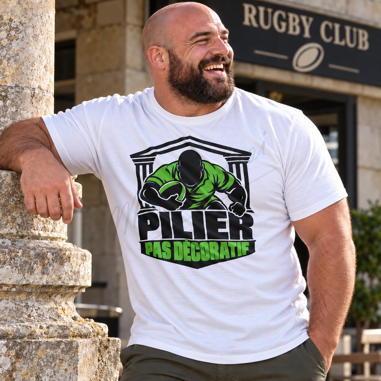 Homme devant un club de rugby portant un t-shirt blanc « Pilier, pas décoratif », avec un motif noir et vert clair sur la poitrine.